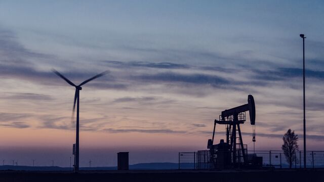 Silhuet af en vindmølle og en olieudvindespumpe i et landskab ved solnedgang.